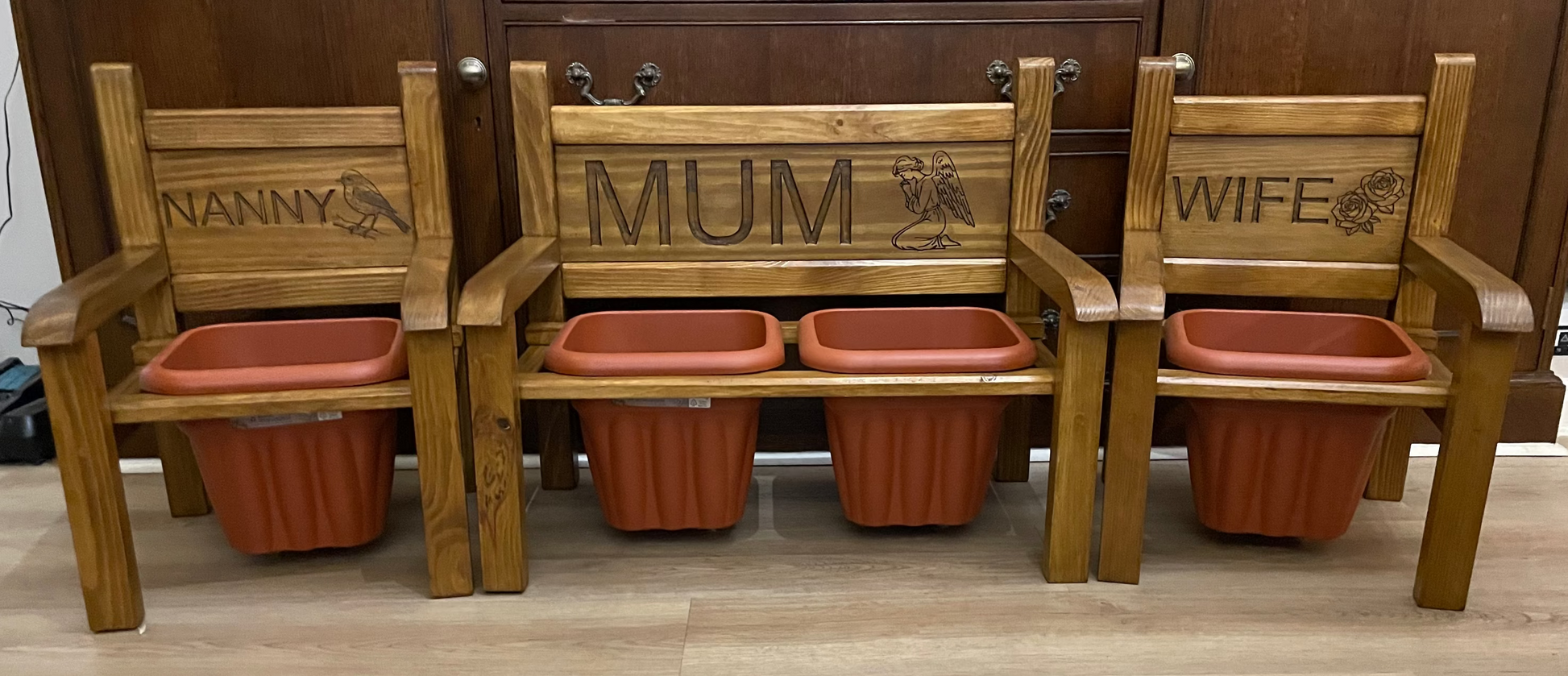 Two flower chairs and 1 flower bench with terracotta pots with 'NANNY', 'MUM', and 'WIFE' on the backrests.