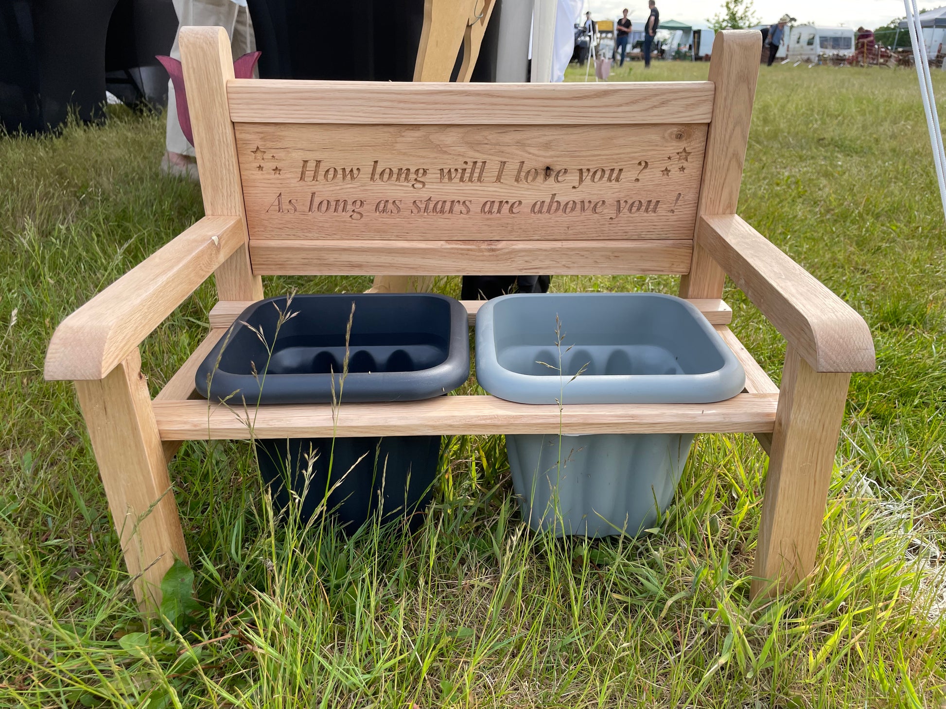 Solid Oak memorial bench set outdoors, featuring two types of grey pots underneath and engraved text on the backrest reading, 'How long will I love you? As long as stars are above you!'.